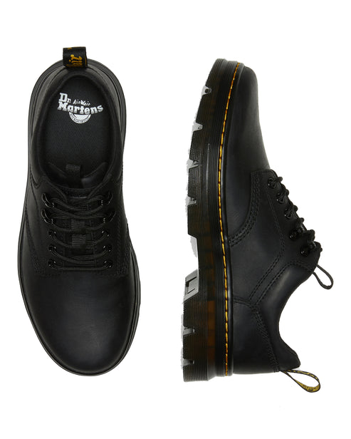 Two matte black lace-up shoes. One shows the toe with a rounded shape and black laces. The other shows the side profile with thick ridged sole and yellow seam.