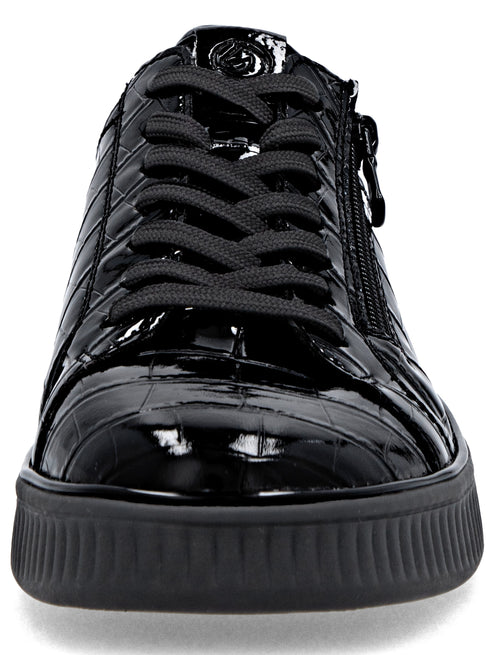 A close-up, front-facing view of a shiny, black sneaker with a textured, crocodile-skin pattern, featuring black laces and a black rubber sole with a vertical ridged design.