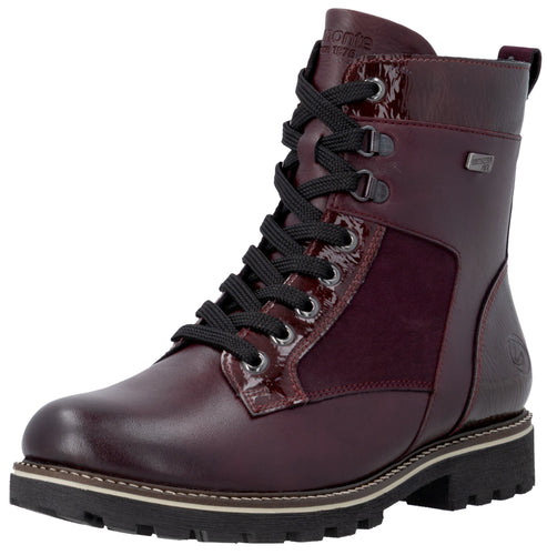A maroon lace-up ankle boot featuring a mix of smooth and textured leather, black laces, a side zipper, and a thick, lugged black rubber sole.