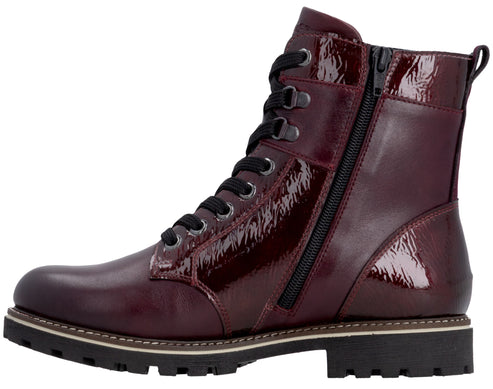 A maroon-colored, lace-up ankle boot with a high-shine patent finish on the upper panels and tongue, featuring a side zipper, black laces, and a thick, lugged, dark brown rubber sole with a light-colored welt.