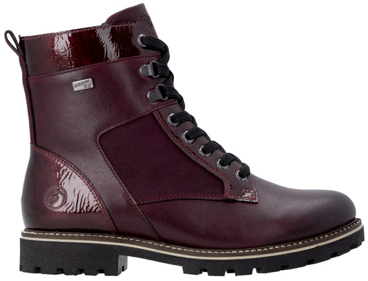 A maroon ankle boot with a lace-up front, a thick black lug sole, and a combination of smooth and patent leather-like panels with black laces and metallic hardware.