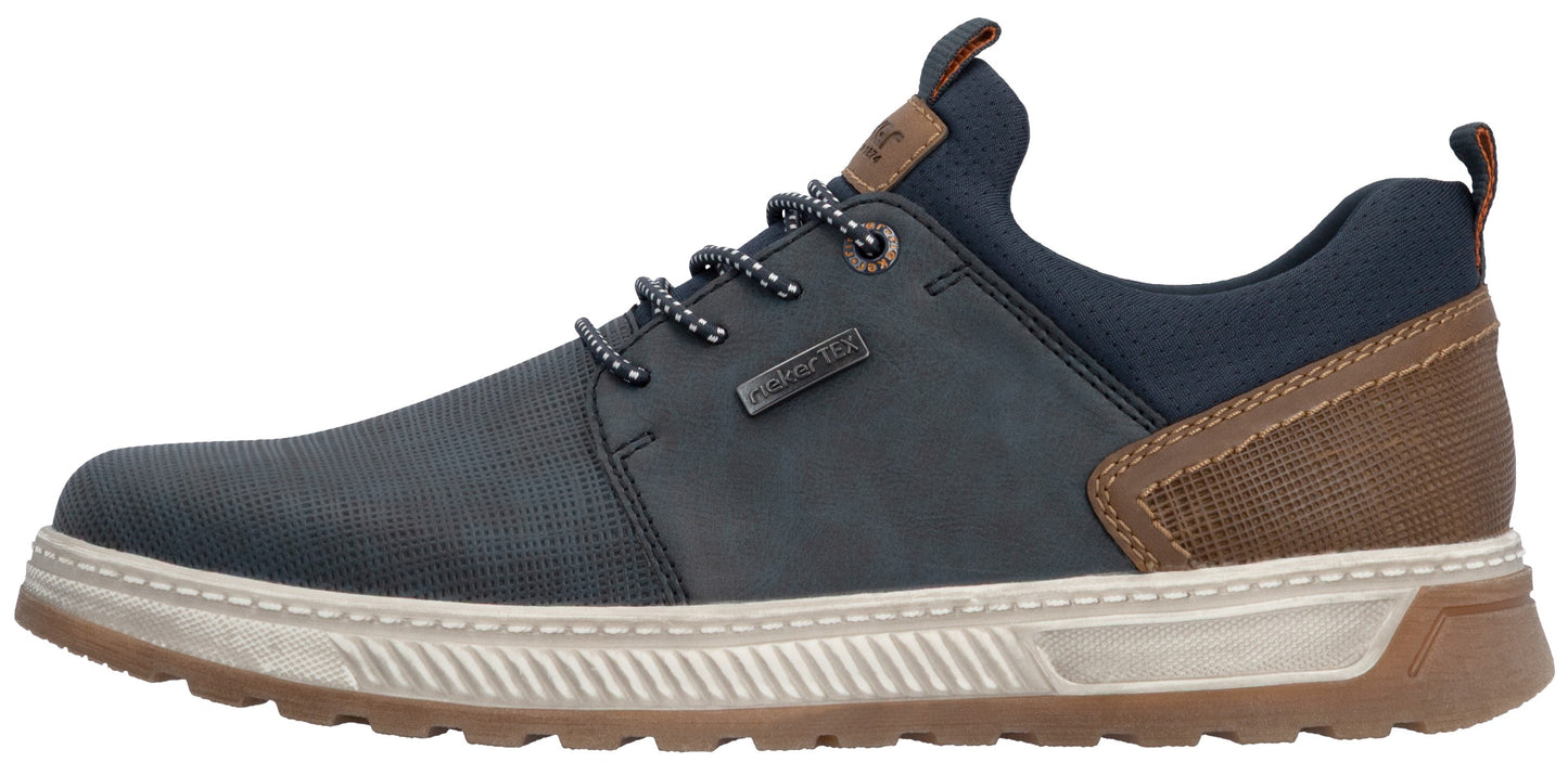 A low-top sneaker featuring a dark navy blue front panel with a micro-perforated texture, a matching solid navy midsection with a small metallic tag, and a brown textured heel overlay. The shoe has grey speckled laces, a thick cream-colored ridged midsole, and a dark brown outsole.