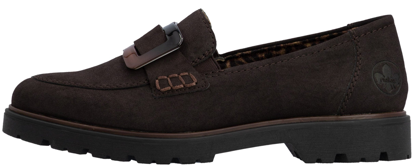 A brown suede slip-on loafer with a thick lug sole, featuring a decorative buckle strap across the instep and visible stitching detail on the side.