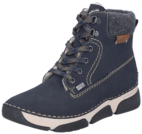 A navy blue ankle boot with a faux fur-lined collar, grey wool-like cuff, metal eyelets, patterned laces, a thick white and black lugged rubber sole, and a visible Rieker Tex tag.