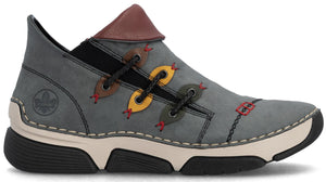 A gray casual shoe with a distinctive asymmetrical lacing system featuring yellow and brown eyelet tabs, a brown collar accent, a light-colored midsole, a thick black ridged outsole, and a debossed logo on the heel.