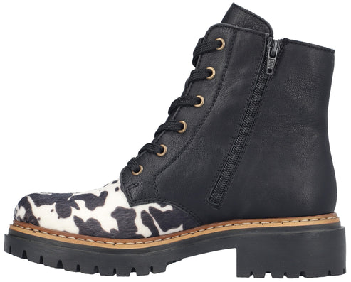 A black ankle boot with a cow-print patterned toe, lace-up front, side zipper, and thick black lug sole.