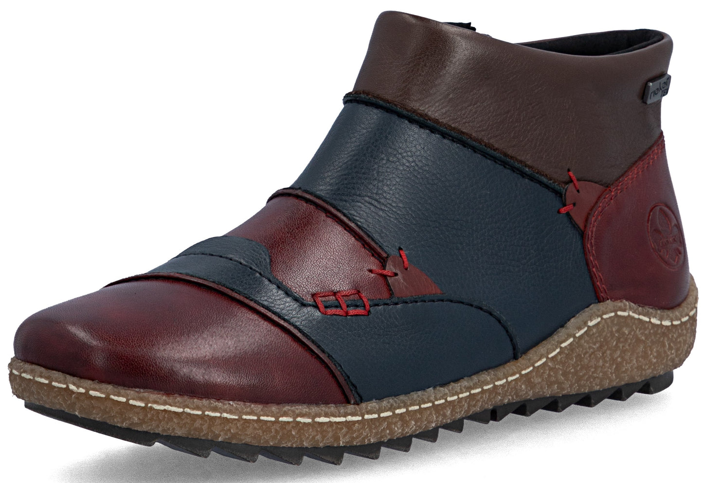 A leather ankle boot with a color-blocked design featuring deep red and navy blue panels, accented by decorative red cross-stitching and a textured, light brown ripple sole with white contrast stitching.