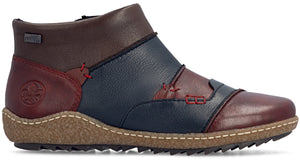 A leather ankle boot with a multi-colored patchwork design, featuring segments of dark red, navy blue, and brown, accented with red stitching, a textured tan rubber sole, and a Rieker logo embossed on the heel.