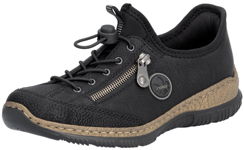 A black slip-on shoe with a textured toe and a tan, stitched midsole. It features an elastic drawstring lacing system and a decorative side zipper with a circular emblem featuring the word 'Rieker'.