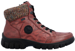 A red ankle boot with a multi-colored knit cuff at the collar, a black lace-up closure with metallic eyelets, and a thick, ridged black rubber lug sole, featuring a circular black logo patch on the side.