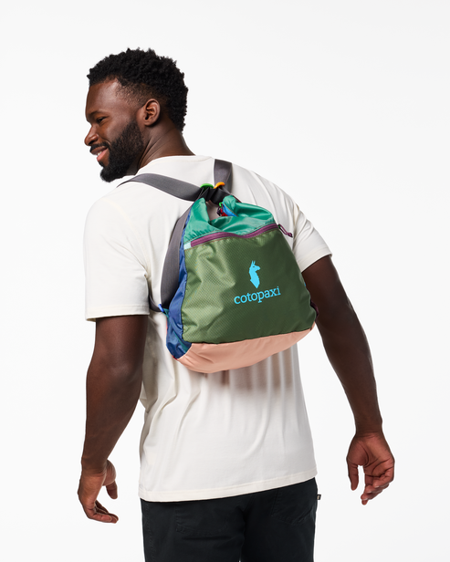 Person wearing small backpack with green, blue, and pink panels and visible text 'cotopaxi'.