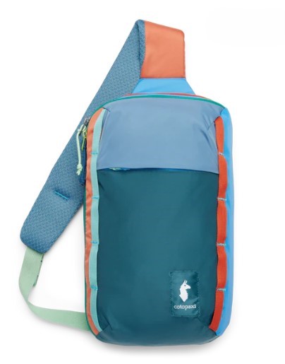 Front-facing, full shot of a sling bag with a single, adjustable shoulder strap. The bag is teal and light blue. The strap is blue with foam pads and an orange top. A green strap is at the bottom. The logo is a llama.