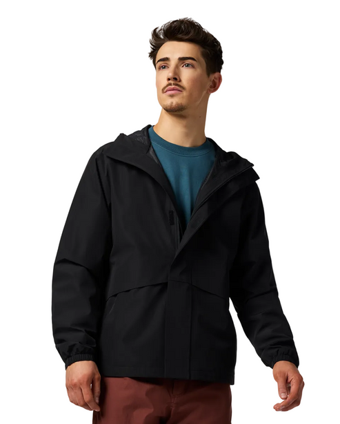 A man is wearing a black jacket with a hood. He has on a blue t-shirt and maroon pants.