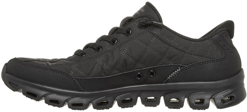 A black quilted low-top athletic shoe with black laces and a thick, segmented black rubber sole featuring open cut-outs for flexibility.