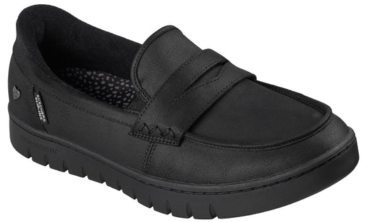 A black loafer shoe with a textured thick sole, a stitched strap across the top, and a visible brand tag on the side.