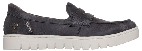 A black slip-on loafer with a thick, textured white sole, featuring a small metallic heart emblem and a small fabric tag reading 'SKECHERS SLIP-INS' on the side.