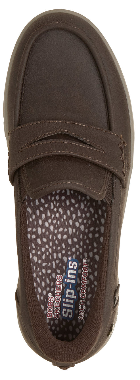 A brown slip-on penny loafer viewed from directly above, featuring a speckled patterned insole with the visible text 'Skechers slip-ins Arch Comfort'.