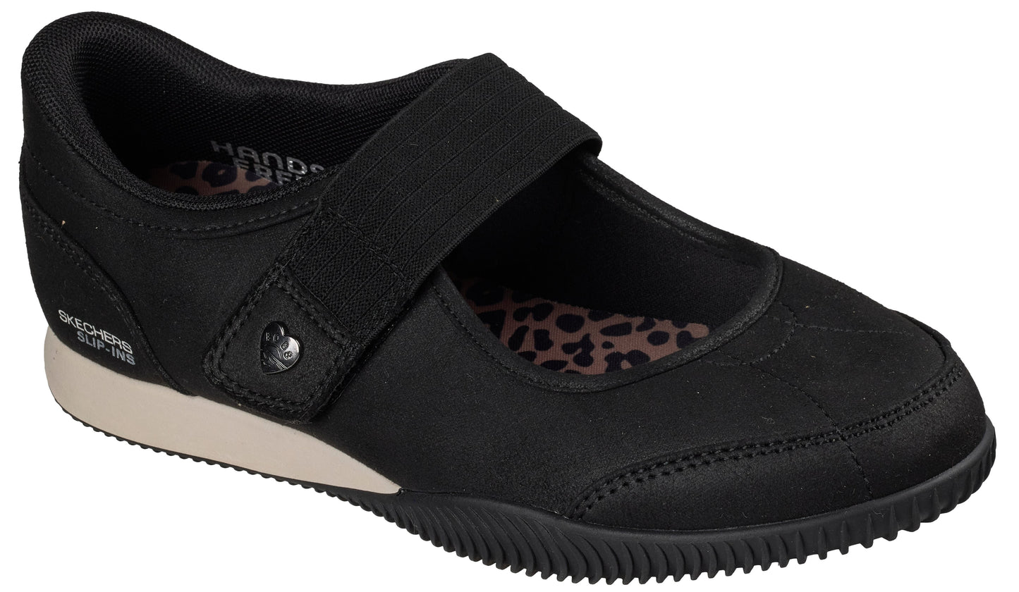A black slip-on Mary Jane shoe with a thick elastic strap, a small heart-shaped accent on the side, a light tan midsole, a textured black rubber outsole, and an interior footbed featuring a black and pink leopard print pattern, with the text 'SKECHERS SLIP-INS' visible on the heel.