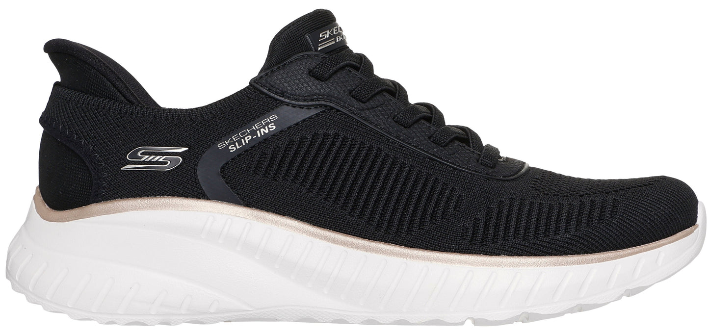 A black Skechers Slip-ins athletic sneaker with a white midsole, a small metallic pink accent between the upper and sole, and the S logo on the side.