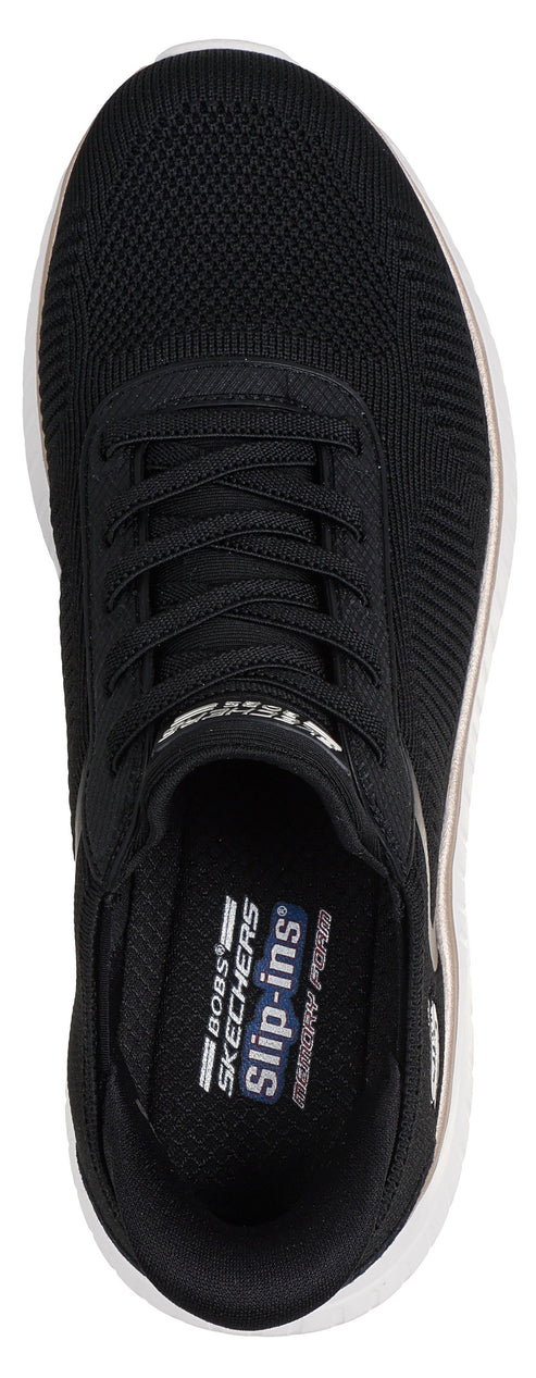 A black Skechers Bobs Slip-ins sneaker seen from a top-down perspective, featuring a knit mesh upper with decorative laces, a white outsole, and an interior footbed marked with the text Bobs Skechers Slip-ins Memory Foam.