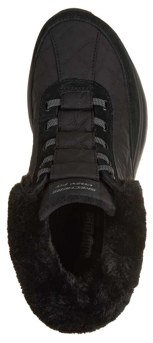 A top-down view of a black slip-on boot featuring a quilted upper, gray elastic lacing, and a plush black faux-fur collar, with the text SKECHERS COZY FIT visible on the tongue.