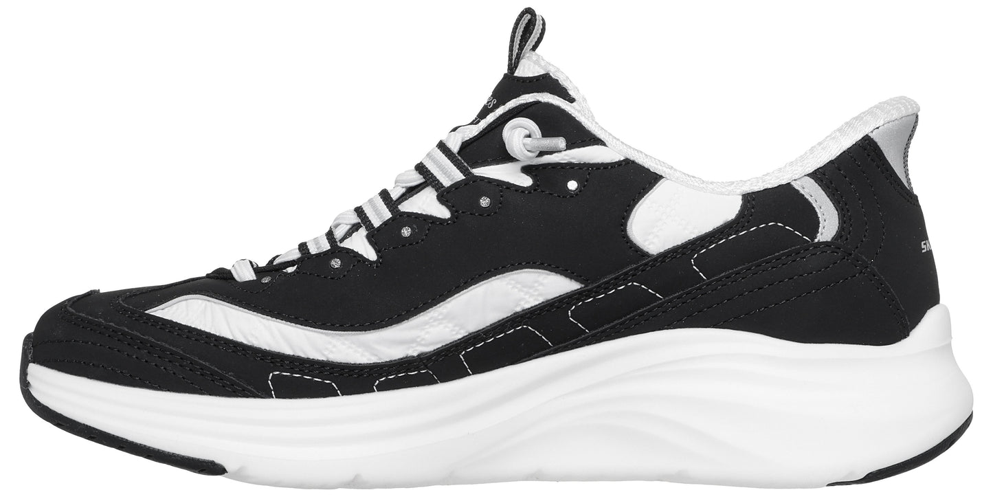 A black and white athletic shoe in profile, featuring a black mesh and suede upper with white overlay accents, a thick white midsole with a wavy design, and a black outsole.