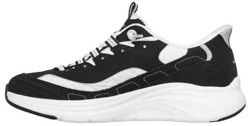 A black and white athletic shoe in profile, featuring a black mesh and suede upper with white overlay accents, a thick white midsole with a wavy design, and a black outsole.