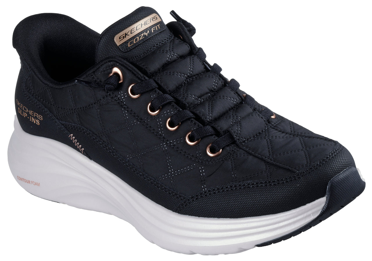 Low-top slip-on black shoe with white sole, rose-gold eyelets, and “COZY FIT” text on the tongue.