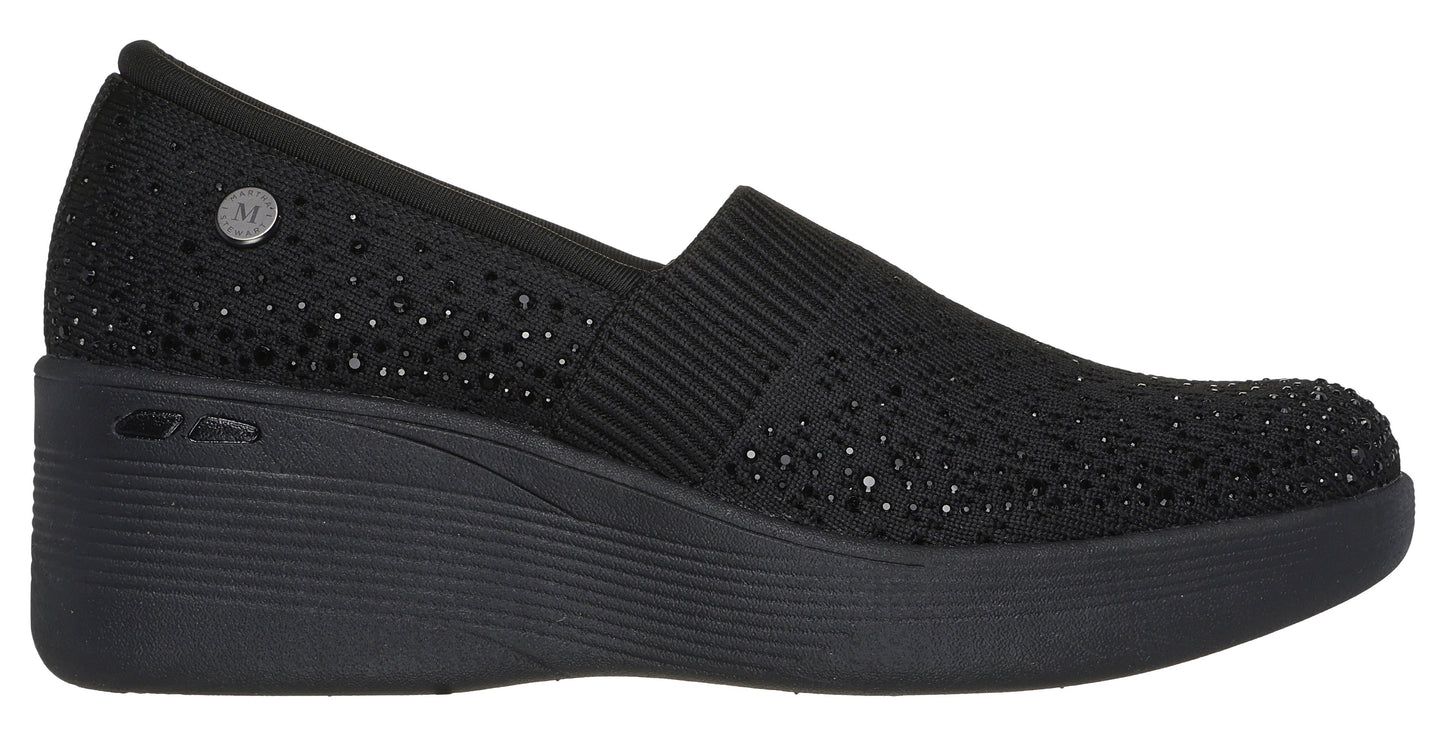 Black wedge slip-on shoe with elastic panel and metallic dots.