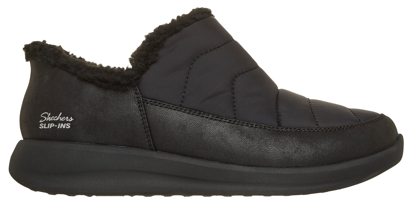 A black slip-on shoe with a quilted upper, faux-fur lined collar, and a thick, textured black rubber sole, with "Skechers SLIP-INS" printed on the heel.