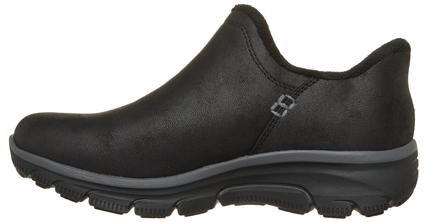 A black slip-on shoe with a rounded toe, a dark grey midsole, and a black, rugged outsole, viewed from the side.
