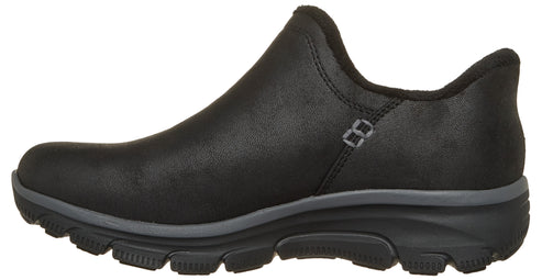A black slip-on shoe with a rounded toe, a dark grey midsole, and a black, rugged outsole, viewed from the side.