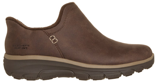 A brown slip-on shoe with a dark brown, thick, textured rubber sole and a beige midsole stripe, featuring the embossed text SKECHERS SLIP-INS on the outer heel area.