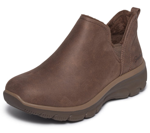 A brown slip-on ankle boot featuring a smooth leather upper, a rounded toe, a soft faux fur lining, and a thick, textured, darker brown rubber sole.