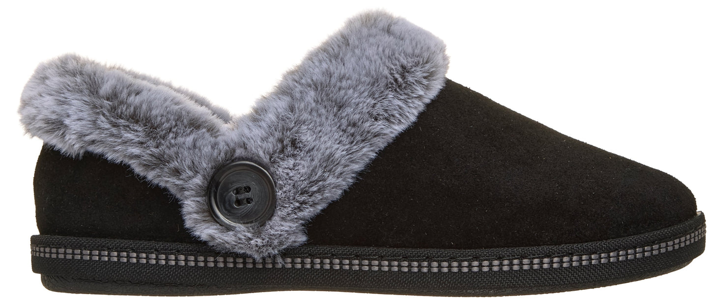A black suede slipper with grey faux fur trim along the collar, accented by a black button on the side and a textured, decorative band around the base.