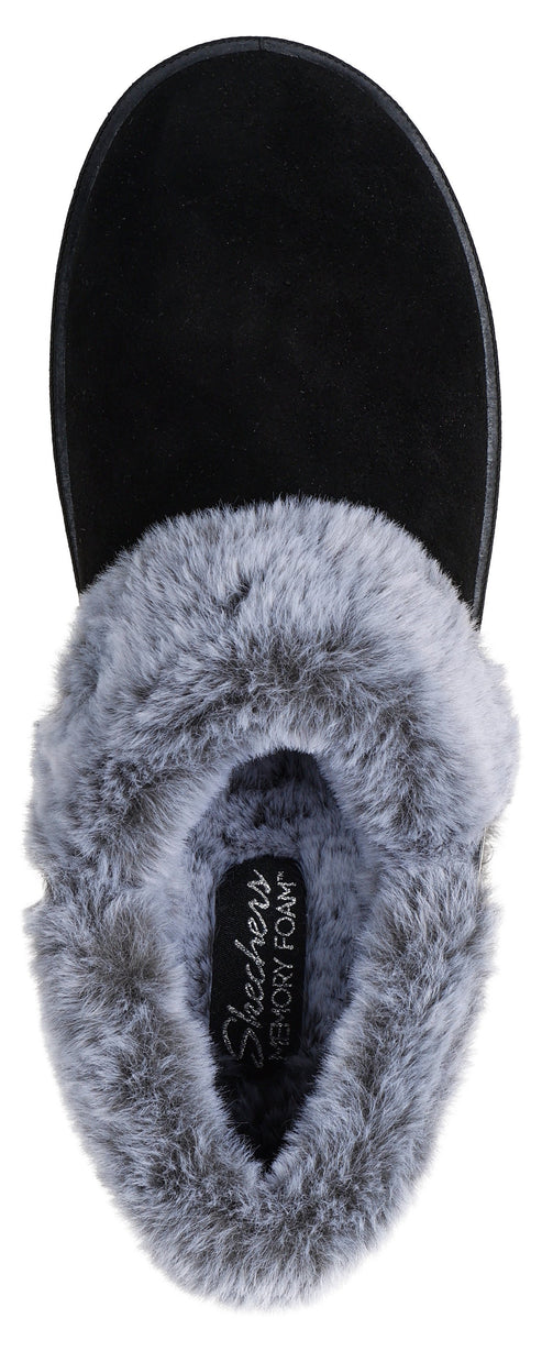 A black slip-on slipper with a grey faux-fur lining and collar, shown from a top-down perspective, with the interior footbed label reading 'Skechers Memory Foam'.