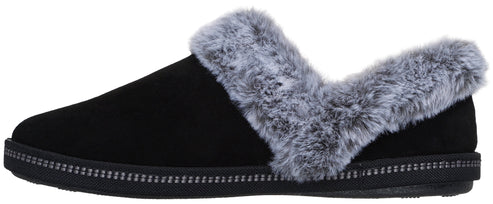 A black slip-on slipper with a grey faux-fur trim lining the opening and a decorative dotted strip along the black sole.