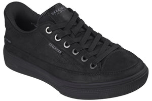 A low-top, all-black sneaker with a canvas upper, a thick rubber midsole, and matching black laces threaded through silver-toned eyelets, featuring the brand name visible on the tongue and side.