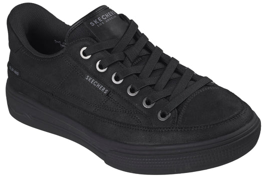 A low-top, all-black sneaker with a canvas upper, a thick rubber midsole, and matching black laces threaded through silver-toned eyelets, featuring the brand name visible on the tongue and side.