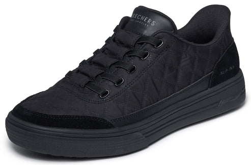 A black Skechers low-top sneaker with a quilted fabric upper, black suede overlays on the toe and heel, thick rubber soles, and tonal black laces.