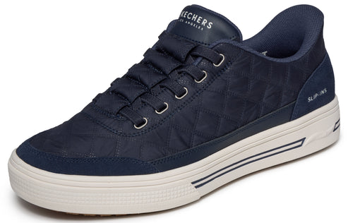 A navy blue low-top sneaker with a diamond-quilted pattern on the upper, matching fabric laces, and a thick off-white sole with dark blue accent stripes and the text "SLIP-INS" visible on the heel.