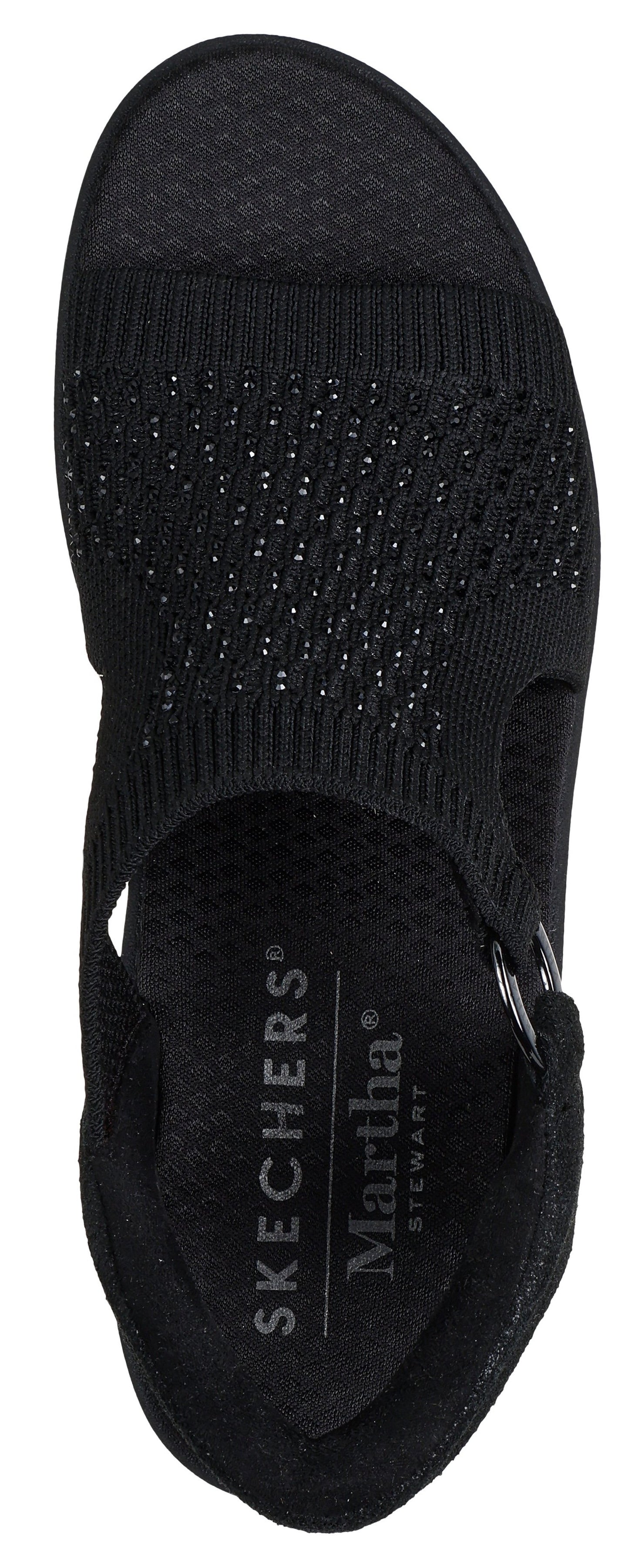 A black sandal with an elastic strap and a flat sole. The insole has white text on it that reads "SKECHERS" and "Martha Stewart".
