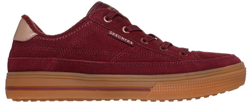 A maroon suede sneaker with a gum rubber sole, featuring a tan heel tab and the brand name "SKECHERS" embossed on the side.