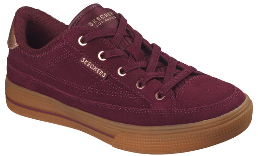 A maroon-colored, low-top lace-up sneaker with a gum-colored rubber sole and a small metallic detail on the heel.