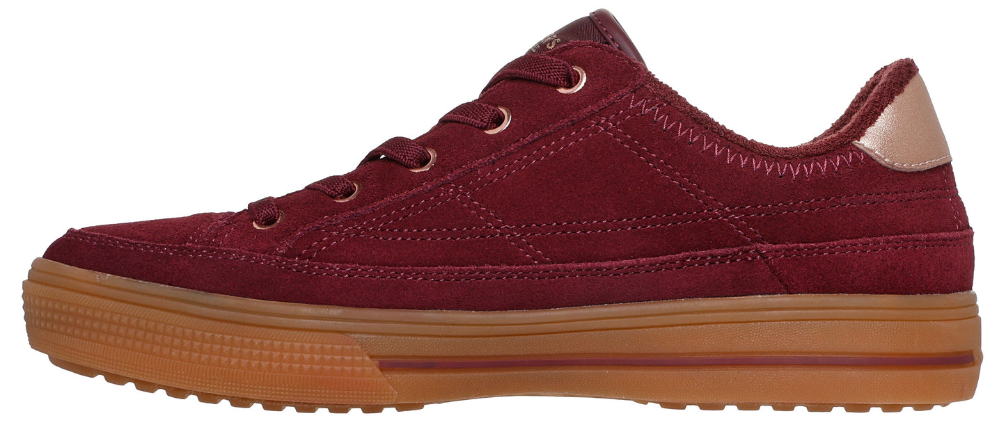 A low-top, burgundy suede sneaker with a gum rubber platform sole and a metallic bronze heel tab, viewed from the side.