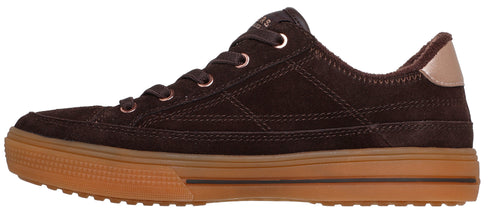 A brown, suede, lace-up sneaker with a flat gum rubber sole, a metallic rose-gold heel tab, and metallic rose-gold lace eyelets.