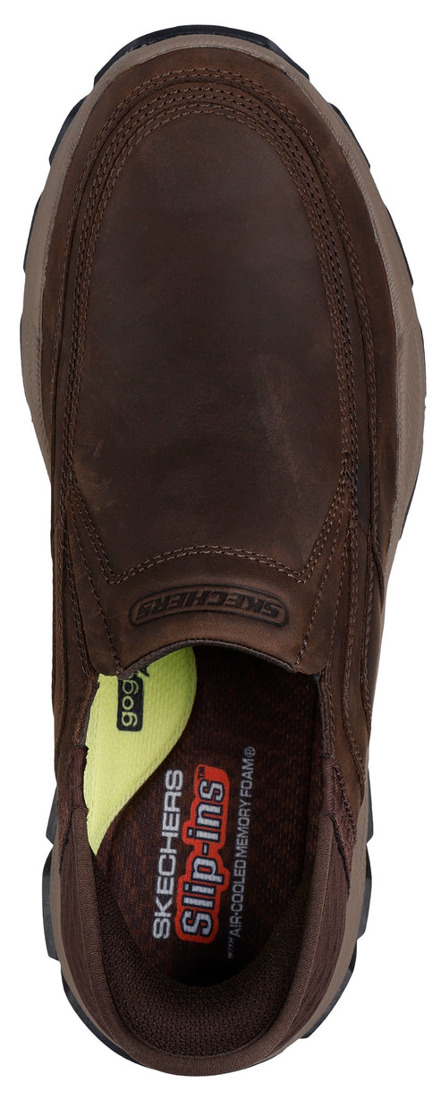 A brown slip-on shoe seen from above, showing a dark brown leather exterior, a dark brown interior lining, and an insole with visible text reading 'Skechers Slip-ins' and 'Air-Cooled Memory Foam', along with a small lime green detail on the side.