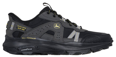 A side view of a dark gray and black athletic shoe with the Goodyear logo on the black sole and a John Deere logo on the side.