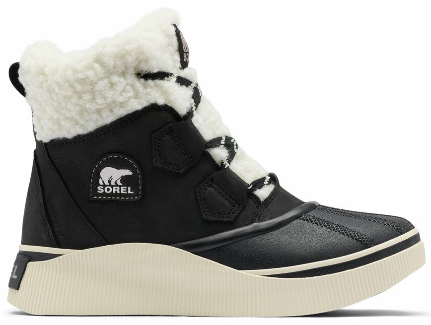 A black Sorel ankle boot with a white fuzzy fleece collar, a white textured platform rubber sole, and a black lace-up front with a Sorel bear logo patch on the side.