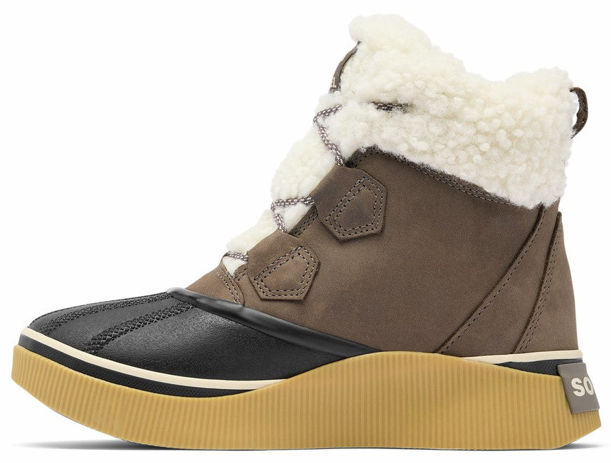 A brown suede and black rubber winter boot featuring a white faux-shearling cuff, cream-colored laces, and a thick, textured tan rubber platform sole, shown from the side.